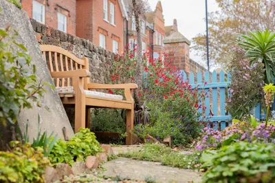a wooden bench sitting in a garden with flowers at Top Step Cottage in Aldeburgh