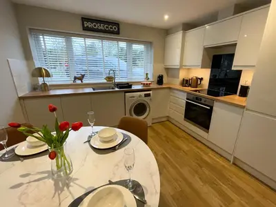 a kitchen with a dining table and a kitchen with white cabinets at Luxury 1 bed new build house near Science & Business parks in Cambridge