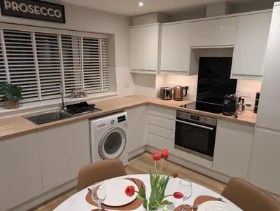 a kitchen with white cabinets and a table with red flowers at Luxury 1 bed new build house near Science & Business parks in Cambridge