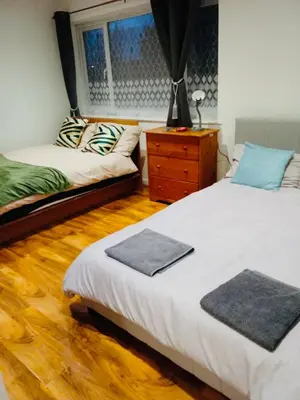 a bedroom with two beds and a dresser and a window at Maxismile Haven in Southend-on-Sea