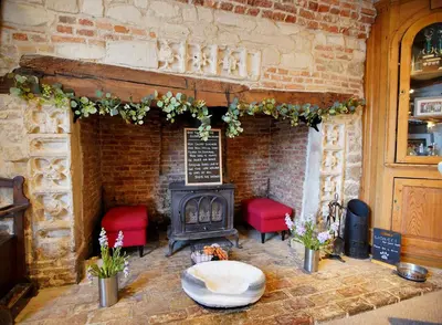 a stone fireplace with red chairs and a stove at The Golden Boar Inn in Freckenham
