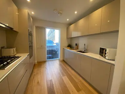 a kitchen with white cabinets and a wooden floor at Autumn House Cambridge free parking in Trumpington