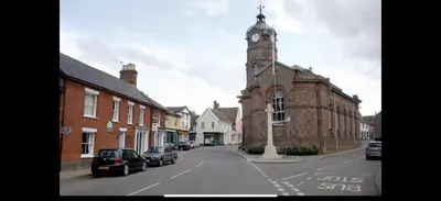 an old brick building with a clock tower on a street at Cosy two bedroom house in eye Suffolk with parking near A140 in Eye