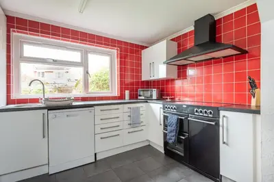 a red tiled kitchen with a stove and a window at Serene 5BR - A Cozy Home Away From Home in Theydon Bois