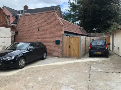 two cars parked in a driveway next to a brick building at Perfitt Place in Bungay
