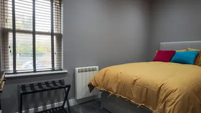 a bedroom with a bed with colorful pillows and a window at Colchester Luxury Apartments - Colonia in Colchester