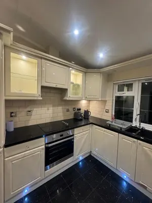 a kitchen with white cabinets and black counter tops at Richard guest house in Roydon