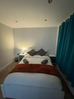 a bedroom with a large white bed with blue curtains at Richard guest house in Roydon