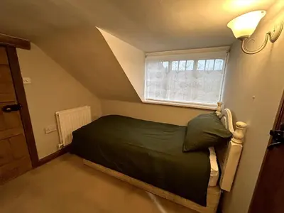 a small bedroom with a green bed and a window at Beautiful Cottage opposite Hedingham Castle! in Castle Hedingham