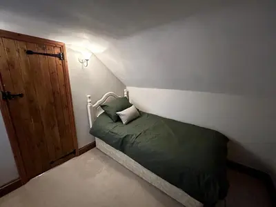 a small bedroom with a bed with a green comforter at Beautiful Cottage opposite Hedingham Castle! in Castle Hedingham