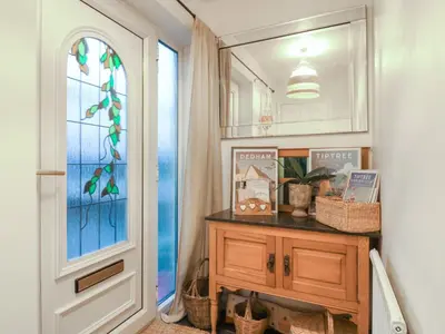 a hallway with a mirror and a wooden dresser and a door at Berkley Cottage in Colchester