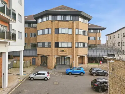 a large brick building with cars parked in a parking lot at Heart of Brentwood - 1 Bed - Underground Parking - Fast Wifi in Brentwood