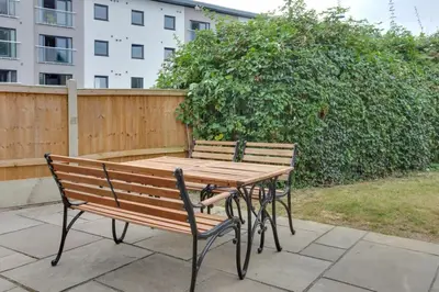 a wooden table and chairs sitting next to a fence at Surehaven Stays 4 Bedroom House Braintree in Braintree