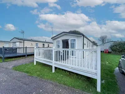 a small white house with a white fence at Lovely 8 Berth Caravan With Decking To Hire At Naze Marine In Essex Ref 17030Ga in Walton-on-the-Naze