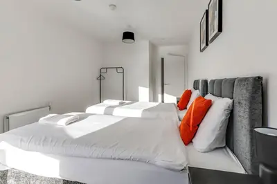 two beds in a white room with orange pillows at The Opulent Property Project ChelmsfordCityCentre 2Bed2Bath FreeParking Balcony in Chelmsford