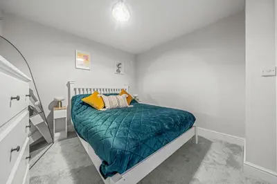 a white bedroom with a bed with a green comforter at College Lane Apartment, Bury St Edmunds in Bury Saint Edmunds