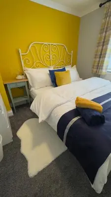 a bedroom with a large bed with a yellow wall at Olivia's Cosy Cottage in Great Baddow