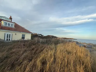 a house on a hill next to the ocean at Cottage on remote wild coast in Bawdsey