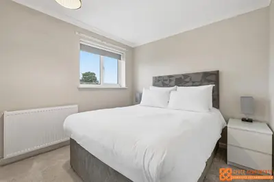 a white bedroom with a large bed and a window at 4 Bed, 2 Bath Detached House, Parking, Fast Wifi in Colchester