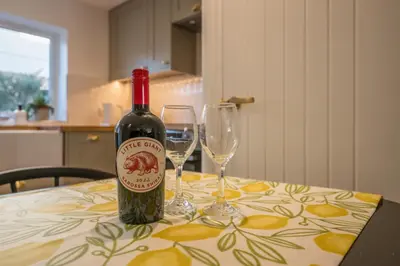a bottle of wine sitting on a table with two glasses at Pink Cottage in Leiston