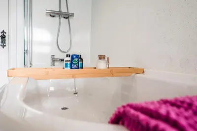a bathroom with a white bath tub with a wooden shelf at The Secret Cottage, Aldeburgh in Aldeburgh