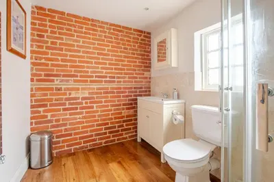 a bathroom with a toilet and a brick wall at Charming Georgian flint cottage in Bury Saint Edmunds