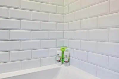 a white tiled bathroom with a bath tub with two bottles at Cosy 2 Bedroom Flat Near Westcliff On Sea Beach & Hamlet Court Road in Southend-on-Sea