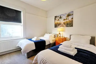a bedroom with two beds and a window with palm trees at Cosy 2 Bedroom Flat Near Westcliff On Sea Beach & Hamlet Court Road in Southend-on-Sea