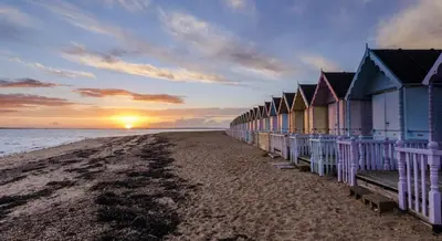 a row of beach huts on the beach at sunset at Digby House flat 1 in West Mersea