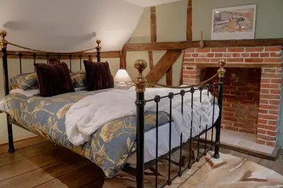a bed in a room with a brick fireplace at The Cotswold Luxe Cottage in Framlingham