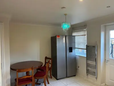 a kitchen with a table and a stainless steel refrigerator at Chartsworth 4 Bedrooms Spacious House in Harold Wood