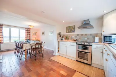 a kitchen with white cabinets and a table with chairs at 1 Box Iron Cottage, Shotley in Shotley
