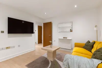 a living room with a yellow couch and a flat screen tv at Khayat Homes - The Ford in Chelmsford