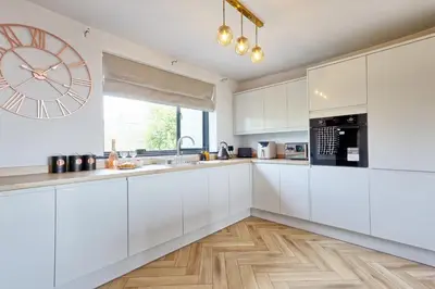 a kitchen with white cabinets and a large clock on the wall at Luxury Apartment- Beach 10mins in Thorpe Bay