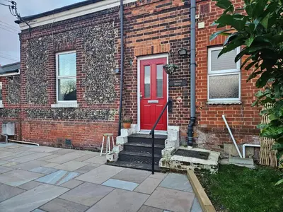 a brick building with a red door and stairs at Station House in Roudham