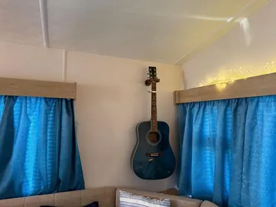 a guitar hanging on a wall in a room with blue curtains at Coastal Beachfront Caravan in Brightlingsea