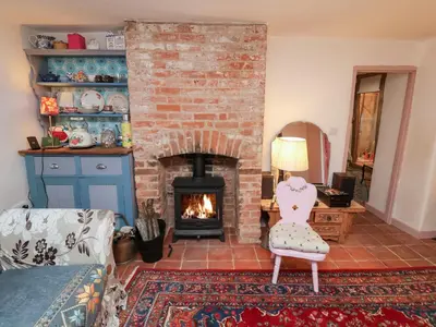 a living room with a fireplace and a chair at The Hare & The Bumblebee Cottage in Eye