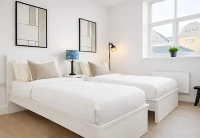 two white beds in a white bedroom with a window at Louisville Flat 3 in Newmarket