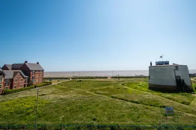 a building on a grassy field next to the ocean at Serene Sands in Felixstowe