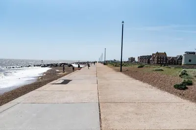a sidewalk next to the beach with people walking on it at Serene Sands in Felixstowe