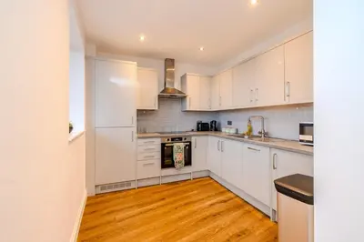 a kitchen with white cabinets and a wooden floor at Lux 2 Bedroom Flt at Brentwood in Brentwood