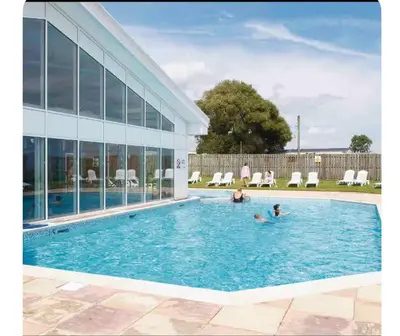 two people in a swimming pool next to a building at A & C Coastal Hideaway with outside Decking in East Mersea
