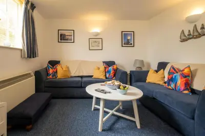 a living room with a blue couch and a table at 1 Ogilvie Lodge - A seafront apartment in Thorpeness - Close to Thorpeness Country Club - Managed by Aldeburgh Coastal Cottages in Thorpeness