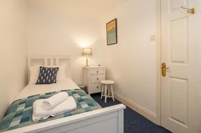 a small bedroom with a bed and a stool at 1 Ogilvie Lodge - A seafront apartment in Thorpeness - Close to Thorpeness Country Club - Managed by Aldeburgh Coastal Cottages in Thorpeness