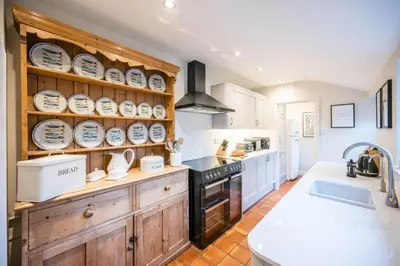 a kitchen with wooden cabinets and plates on the shelves at 7 Highbury Cottages, Leiston in Leiston
