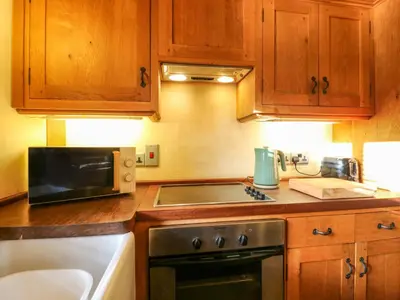 a kitchen with wooden cabinets and a stove and a microwave at The Old Cow Shed in Eye