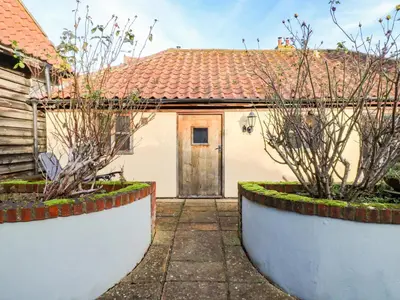 a white house with a door and two bushes at The Old Cow Shed in Eye
