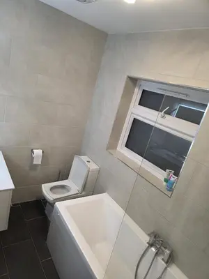 a bathroom with a toilet and a tub and a window at Optimal Homes in Harold Wood