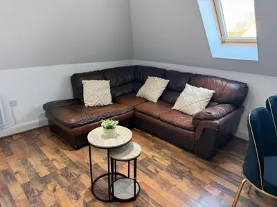 a brown leather couch in a living room with a table at Two-Bedroom Attic House in Colchester