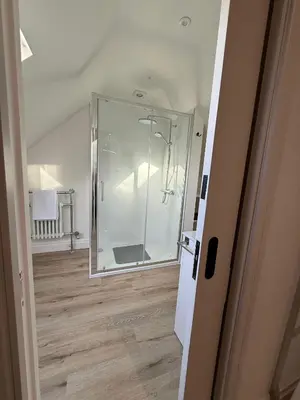 a glass shower in a room with a wooden floor at The Coach House in Halstead